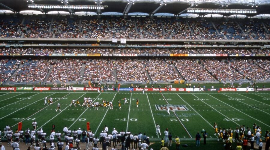 A professional NFL 2025 football game in progress at a large outdoor stadium filled with spectators; both teams are lined up on the field.