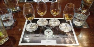 Four whiskey glasses with amber liquid rest on a Jameson-branded tasting mat, surrounded by water glasses on a wooden table—a classic scene often enjoyed during Ireland West tours.