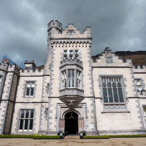 A large stone castle with a central tower and arched entrance, featuring detailed windows and battlements under a cloudy sky—a highlight on many Ireland West tours.