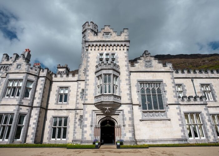 A large stone castle with a central tower and arched entrance, featuring detailed windows and battlements under a cloudy sky—a highlight on many Ireland West tours.
