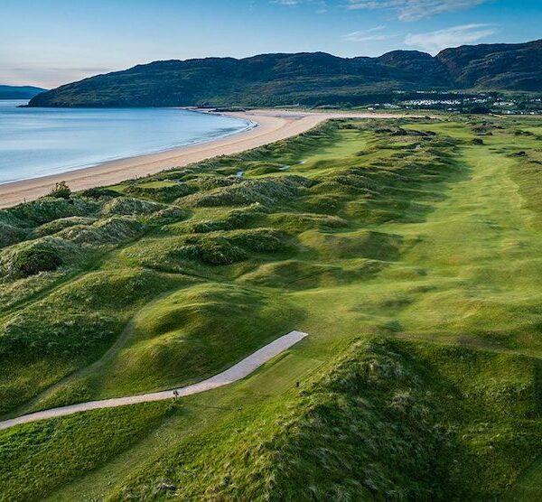 Aerial view of Northwest Links Golf, a stunning coastal golf course with rolling green fairways, sandy dunes, a beach, and hills in the background under a clear sky—an unforgettable highlight of the Golf Series by Lally Tours.