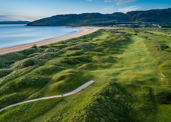 Aerial view of Northwest Links Golf, a stunning coastal golf course with rolling green fairways, sandy dunes, a beach, and hills in the background under a clear sky—an unforgettable highlight of the Golf Series by Lally Tours.