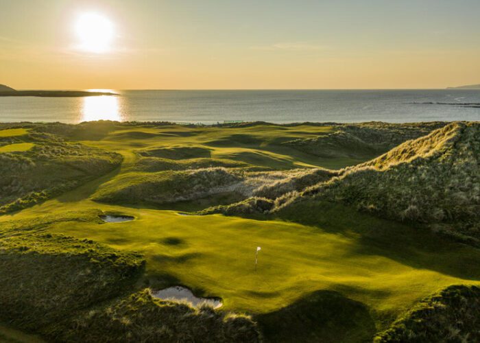 An Irish Links Golf course with rolling greens and sand traps sits beside the ocean at sunset, sunlight casting long shadows over the breathtaking landscape.
