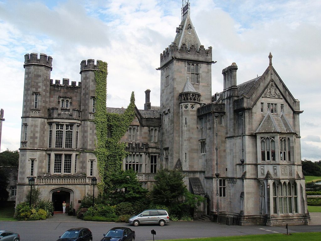 Stone castle with a tall tower and ivy-covered walls, with cars parked in front during an Ireland golf trip.