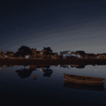 A wooden boat floats on calm water at twilight, reflecting the buildings and streetlights of Galway City, a popular destination for any walking tour.