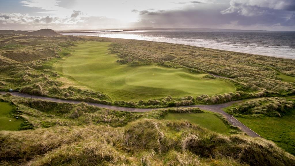 Aerial view of a golf course hole winding through coastal dunes next to the ocean, an iconic setting for an Ireland golf trip.