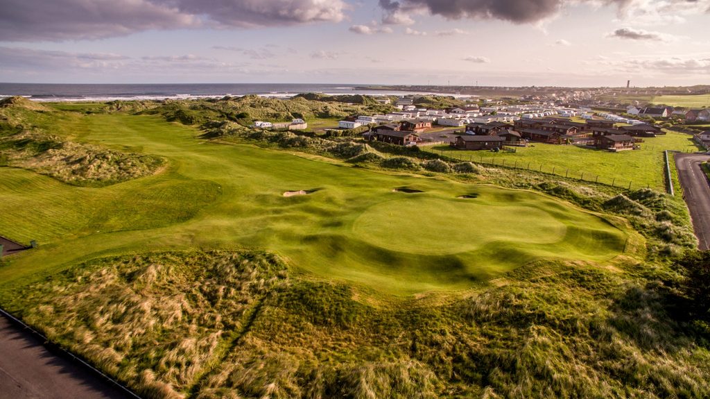 An aerial view of a golf course green situated near a coastal holiday park and the ocean, perfect for an Ireland golf trip.